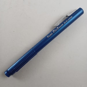 May include: A blue Pentel Clic Eraser ZE-21 Japan. The eraser has a rectangular shape with a ridged grip section and a clear plastic clip. The text "Pentel Clic Eraser ZE-21 JAPAN" is printed on the side.