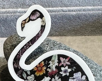 May include: A white outline of a flamingo with a floral pattern inside. The flowers are in shades of pink, purple, white, and yellow on a black background.