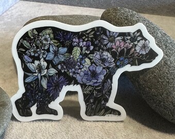 May include: A black bear silhouette sticker with a floral design featuring blue, purple, and white flowers on a black background.