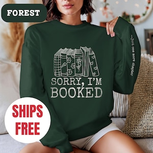 May include: A dark green sweatshirt with a white graphic of stacked books and the text "Sorry, I'm Booked." The text "...Just one more chapter" is printed on the sleeve.