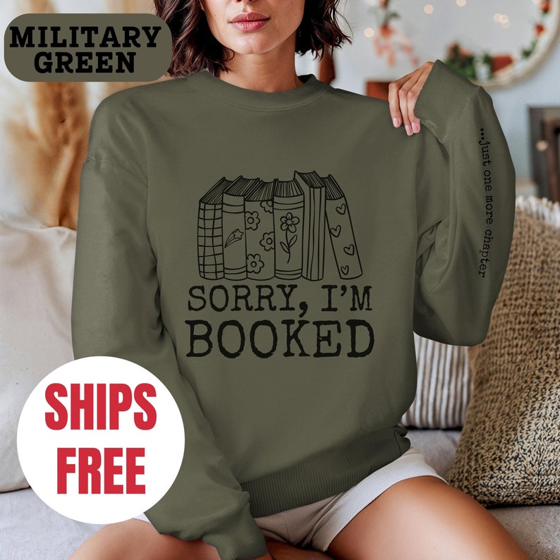 May include: A green sweatshirt with the text "Sorry, I'm Booked" and a stack of books with flowers and hearts. The text "...just one more chapter" is on the sleeve.