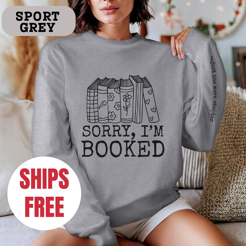 May include: A gray sweatshirt with a stack of books and the text "Sorry, I'm Booked" and "...just one more chapter" on the sleeve.