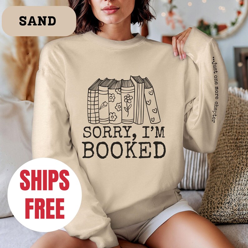 May include: A beige sweatshirt with a graphic of stacked books and the text "Sorry, I'm Booked" and "...just one more chapter".