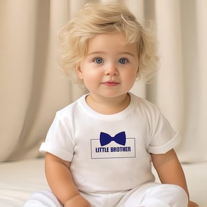 May include: A white baby onesie with a blue bow tie and the text "LITTLE BROTHER" in a blue rectangle.