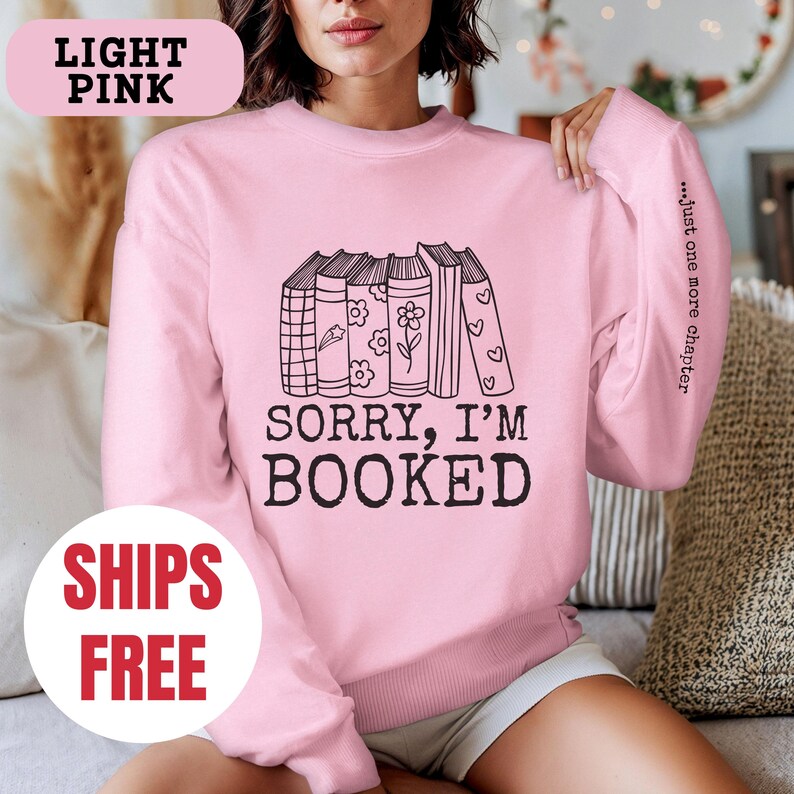 May include: Light pink sweatshirt with a stack of books and the text "Sorry, I'm Booked" and "...just one more chapter" on the sleeve.