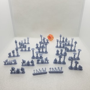May include: A collection of 3D printed miniature candle holders and other decorative items in a light grey colour. The items are arranged on a white surface. There is a red and gold dice in the background.