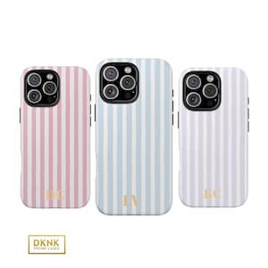 May include: Three smartphone cases featuring vertical stripes in pastel pink, light blue, and soft lavender. Each case has a black camera cutout and gold-colored initials at the bottom. A small rectangular logo at the bottom reads DKNK PHONE CASES.