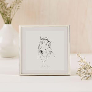 K&ouml;nnte beinhalten: Ein gerahmter Kunstdruck mit einer Strichzeichnung eines Hundes mit Hut und Schal. Der Name des Hundes, "COOKIE", steht unter dem Bild. Der Rahmen ist silberfarben, der Hintergrund ist neutral.