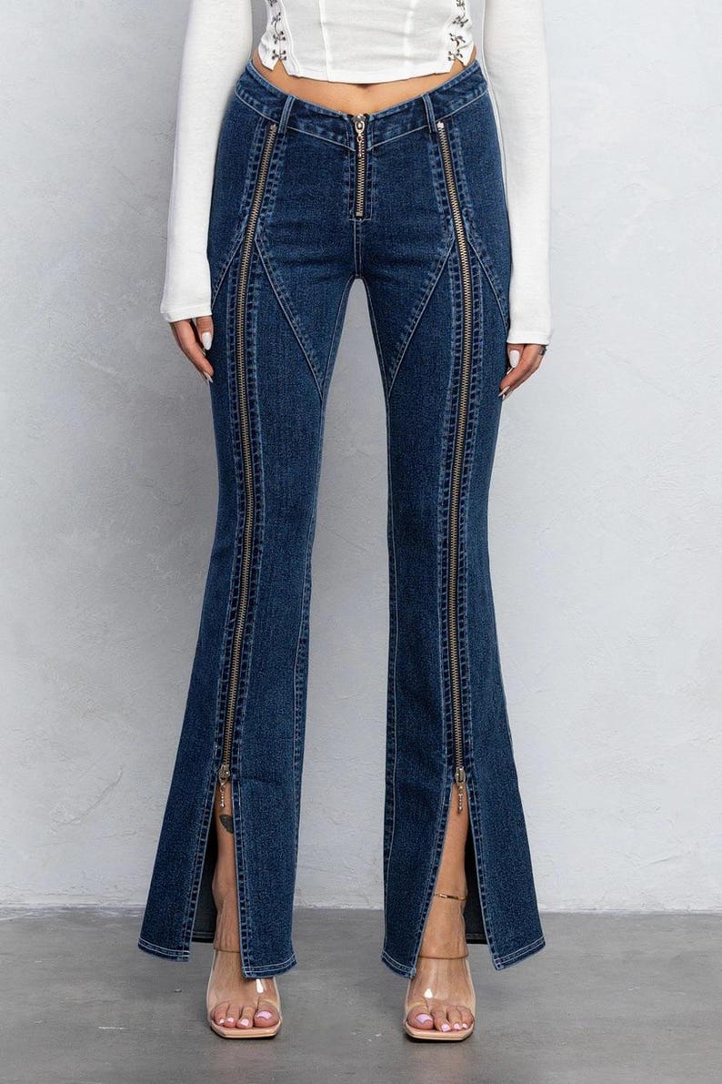 Pu&ograve; includere: Jeans in denim blu con pi&ugrave; dettagli di cerniera sulle gambe. I jeans hanno uno stile a gamba svasata.