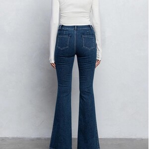 Pu&ograve; includere: Un paio di jeans in denim blu scuro con gamba a campana. I jeans hanno vita alta e chiusura con zip.