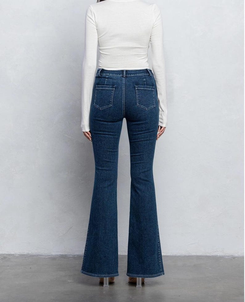 Pu&ograve; includere: Un paio di jeans in denim blu scuro con gamba a campana. I jeans hanno vita alta e chiusura con zip.