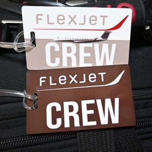 May include: Two brown luggage tags with white text that reads "Flexjet Crew". The top tag has a small image of a white airplane with red accents.