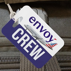 May include: White luggage tag with blue and white text that reads "envoy" and "CREW". A small airplane with the text "American Eagle" is printed on the tag.