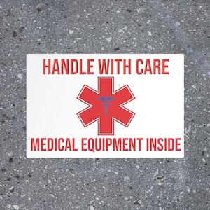May include: White sticker with red text that reads "HANDLE WITH CARE" and "MEDICAL EQUIPMENT INSIDE". A red star of life symbol is in the center of the sticker.