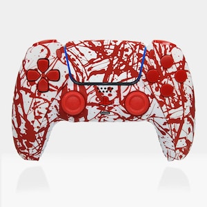Puede incluir: Un mando de PlayStation 5 blanco y rojo con un diseño de pintura salpicada. El mando tiene botones rojos y sticks analógicos rojos.