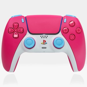 以下が含まれることがあります： ピンクと白の PlayStation 5 コントローラーで、ボタンは青色です。コントローラーの前面には PlayStation のロゴがあります。