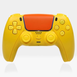 May include: A yellow PlayStation 5 DualSense wireless controller with orange faceplates. The controller has a PlayStation logo and a speaker on the front.