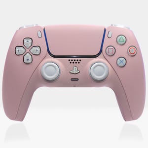 Peut inclure: Une manette sans fil PlayStation 5 DualSense rose avec des boutons blancs et un accent bleu autour du pavé tactile.