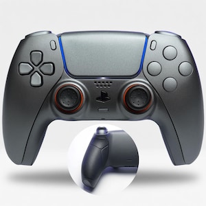 Könnte beinhalten: Ein metallic-dunkelgrauer Videospiel-Controller mit zentralem Touchpad, Steuerkreuz, vier runden Aktionstasten und zwei Analogsticks mit orangefarbenen Ringen. Ein kreisförmiger Ausschnitt zeigt den texturierten schwarzen Griffbereich.