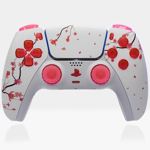 May include: A white PlayStation 5 DualSense controller with a pink cherry blossom design. The controller has pink buttons and pink analogue sticks.