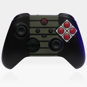 Peut inclure: Une manette Xbox noire avec un design rétro vert et gris. La manette a des boutons rouges avec des lettres blanches qui épellent "A", "B", "X", et "Y".
