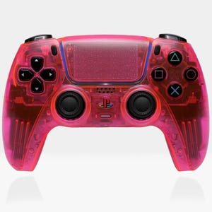 May include: A translucent hot pink video game controller featuring a central touchpad with a visible circuit board pattern, two black analog sticks, a directional pad, four action buttons with geometric symbols, and a PlayStation logo.