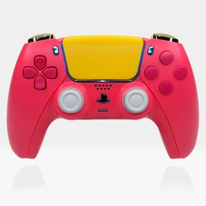 May include: A pink and yellow PlayStation 5 DualSense controller with gold accents. The controller has a yellow faceplate and pink buttons.