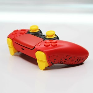 May include: A red and black PlayStation 4 controller with yellow buttons and a black speckled design.