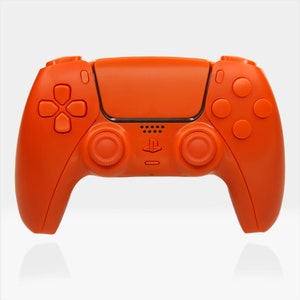 May include: An orange PlayStation 5 DualSense wireless controller with a black PlayStation logo. The controller has a textured grip and a built-in microphone.