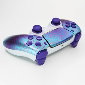 May include: A white PlayStation 4 controller with a blue and purple gradient design and pink lines. The controller has purple buttons and a purple analog stick.