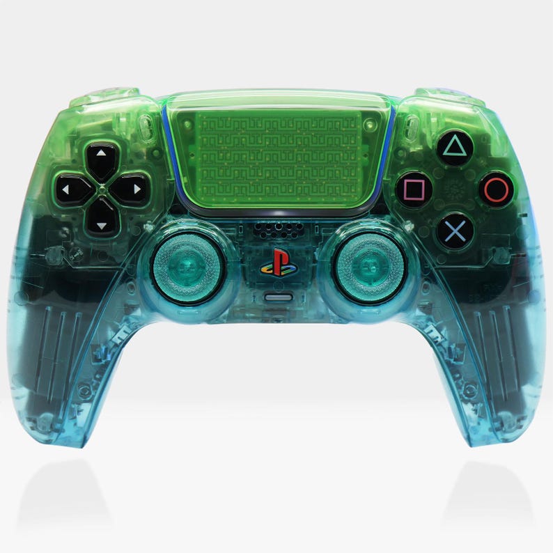 Peut inclure: Une manette de jeu vid&eacute;o transparente verte et bleue avec des boutons noirs et un logo PlayStation. La manette a un design clair et transparent, mettant en valeur les composants internes. Les boutons sont noirs, rouges, bleus et verts.