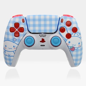May include: A white and blue gingham patterned PlayStation 5 DualSense controller with red buttons and a cartoon character design. The character is a white and pink dog with a red bow and a strawberry.