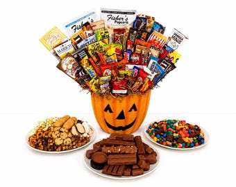 Puede incluir: Un cubo de calabaza de color naranja brillante lleno de un surtido de paquetes de snacks y dulces coloridos. Tres platos blancos están dispuestos delante, uno con galletas y pretzels, otro con barritas de chocolate y otro con caramelos.