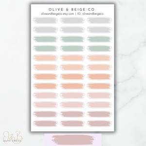 May include: A sheet of 30 pastel-colored brushstroke stickers. The stickers are in shades of gray, green, peach, and pink. The stickers are arranged in rows of five. The sheet is labeled "Olive & Beige Co."
