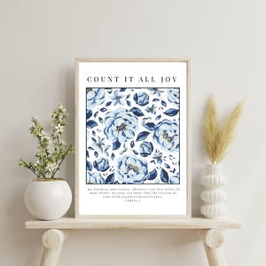 May include: A framed print with the text "COUNT IT ALL JOY" at the top. The print features a floral pattern in shades of blue on a white background. The bottom of the print has text from James 1:2-3. The frame is a light wood color.