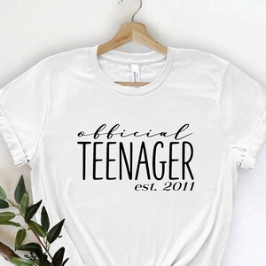May include: White t-shirt with black text that reads "official teenager est. 2011".