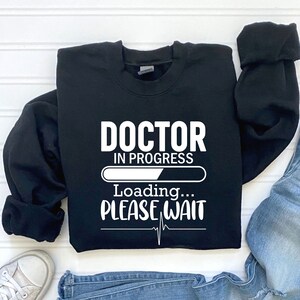 May include: Black sweatshirt with white text that reads "Doctor in Progress Loading... Please Wait" with a progress bar and a heartbeat symbol.