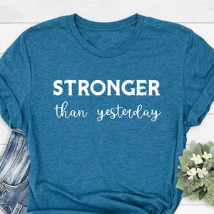 May include: A teal blue t-shirt with the text "STRONGER than yesterday" printed in white.