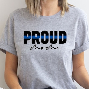 以下が含まれることがあります： 「PROUD mom」という黒い文字が書かれたグレーのTシャツ。PROUDの上には細い青い線が引かれている。