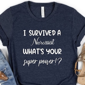 May include: A navy blue t-shirt with white text that reads "I survived a Narcissist What's your super power!?"