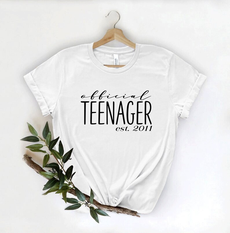 May include: White t-shirt with black text that reads "official teenager est. 2011".