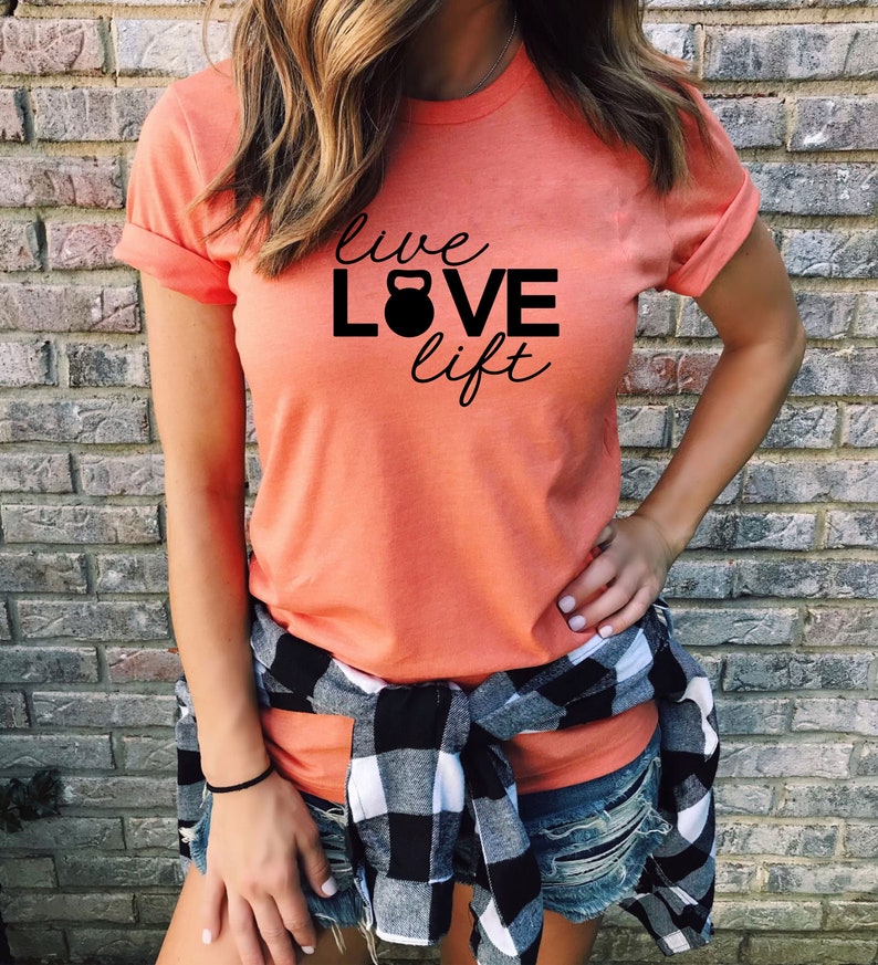 May include: A coral colored t-shirt with the text "live LOVE lift" in black with a black kettlebell graphic between the words "LOVE" and "lift".