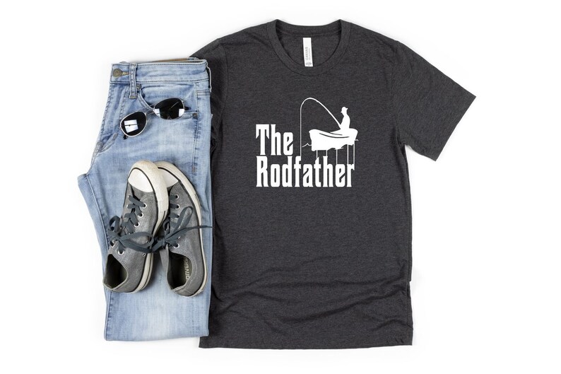 May include: A dark heather grey t-shirt with a white graphic of a person fishing from a boat. The text "The Rodfather" is printed below the graphic.
