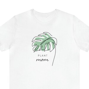 May include: White t-shirt with a green leaf illustration and the text "PLANT mom" printed on the front.