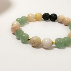 May include: A green, yellow and pink beaded bracelet with two black lava rock beads. The bracelet is made with natural stones and has gold spacers between the beads.