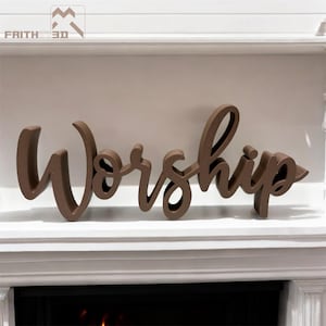 May include: A brown, three-dimensional script sign featuring the word "Worship" in a cursive font. The letters are connected and have a smooth, matte finish. A small logo with the text "FAITH IN 3D" is visible in the upper left corner.
