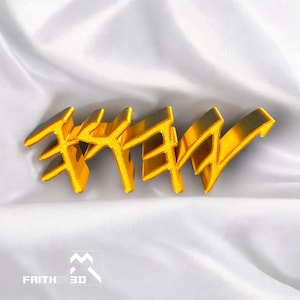 May include: A gold-colored 3D printed word "FREY" on a white fabric background.