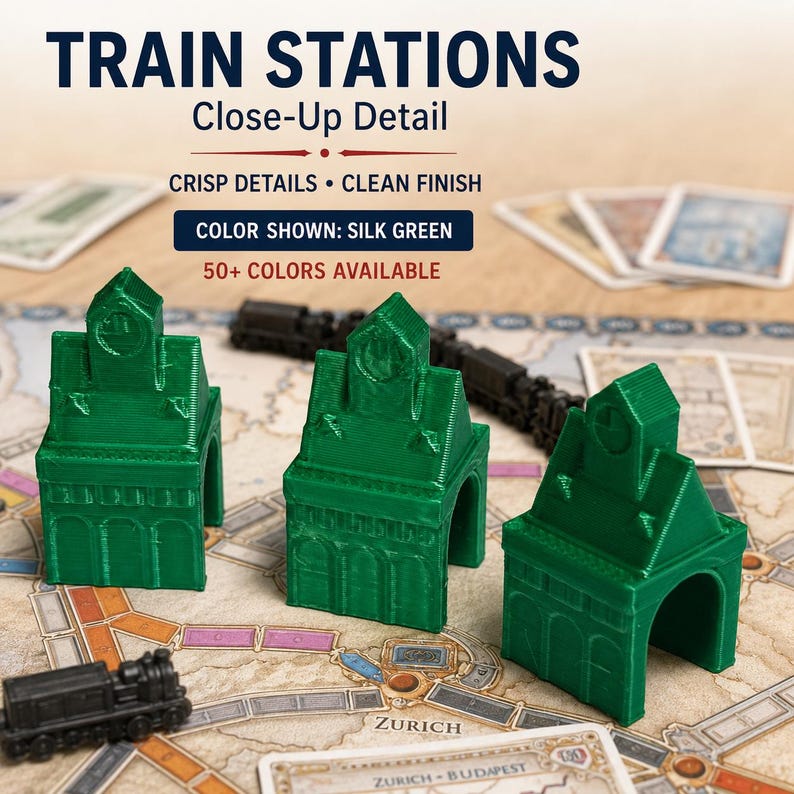 May include: Three silk green 3D-printed train station game pieces with arched doorways and clock tower details. Text on the image reads: TRAIN STATIONS, Close-Up Detail, CRISP DETAILS &bull; CLEAN FINISH, COLOR SHOWN: SILK GREEN, 50+ COLORS AVAILABLE.