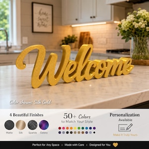 Peut inclure: Une enseigne autoportante affichant le mot Welcome dans une police cursive avec une finition or soie. L'enseigne est posée sur un comptoir. Sous l'enseigne, le texte indique Color shown: Silk Gold, 4 Beautiful Finishes et Personalization Available.