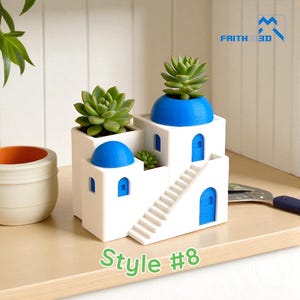 Può includere: Una fioriera architettonica in miniatura bianca e blu con un design di isola greca, contenente piante grasse verdi. La fioriera presenta cupole, porte e finestre blu, con una scala. Il testo "Style #8" è in basso.